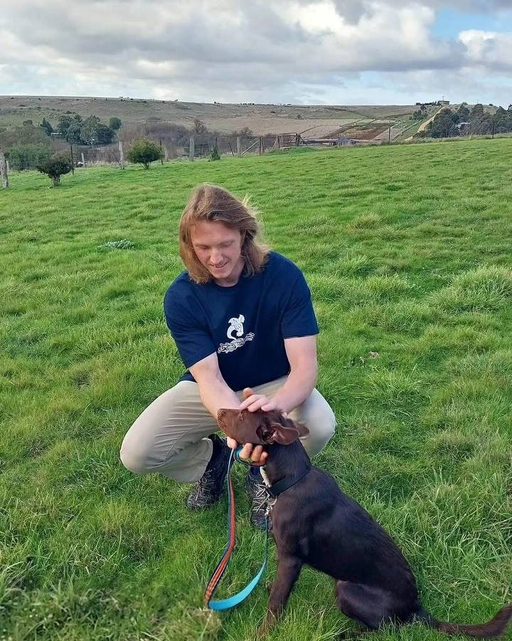 James crouching in a grassy paddock with Bunji on the lead